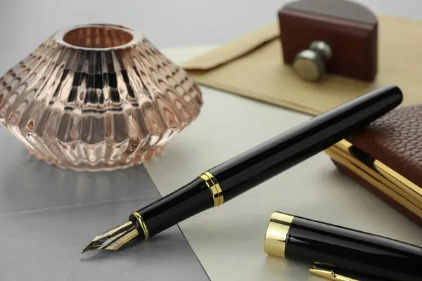 Stylish fountain pen, inkwell and paper on grey textured table, closeup