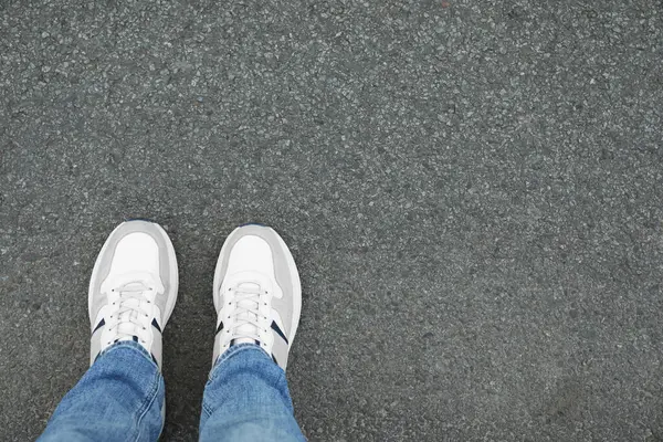 Man in sneakers standing on asphalt, top view. Space for text