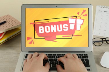 İkramiye kazanıyor. Ahşap masada dizüstü bilgisayar kullanan bir kadın, yakın plan. Aygıt ekranında hediye kutusu ve sözcüğün görüntüsü