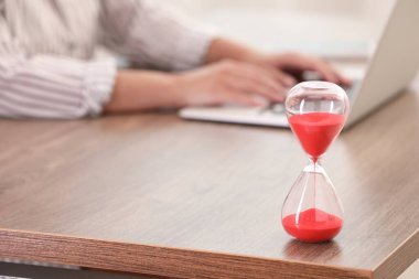 Masada kırmızı kum akan kum saati. İçerde dizüstü bilgisayar kullanan kadın, yakın plan.