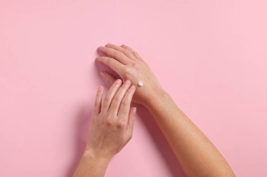 Kadın pembe arka planda kozmetik krem sürüyor.