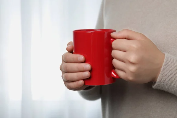 Woman holding red mug indoors, closeup view