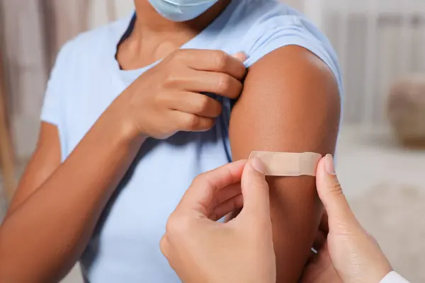 Doctor putting adhesive bandage on young woman\'s arm after vaccination indoors, closeup