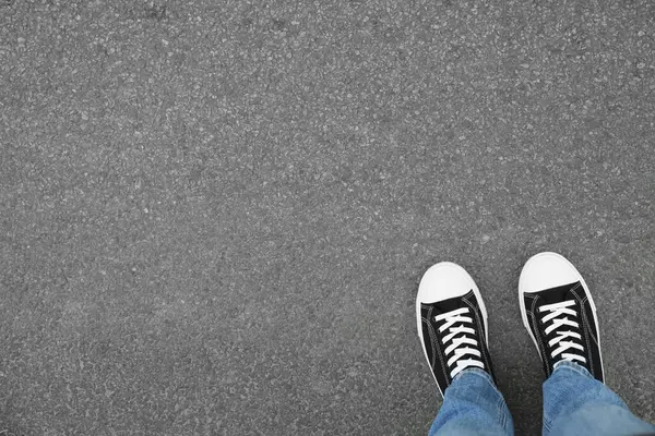 Man in sneakers standing on asphalt, top view. Space for text