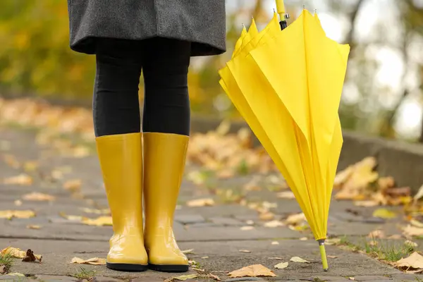 Woman with yellow umbrella and rubber boots in autumn park, closeup