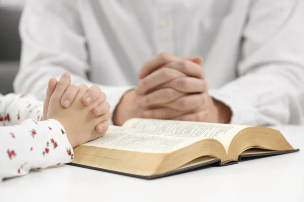Girl and her godparent praying over Bible together at table indoors, closeup
