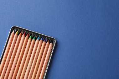 Mavi arka planda bir sürü renkli pastel kalemli kutu, üst görünüm ve metin için boşluk. Malzemeler çiziliyor