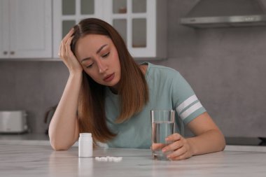 Mutfaktaki masada bir bardak su ve antidepresan haplı depresyondaki kadın.