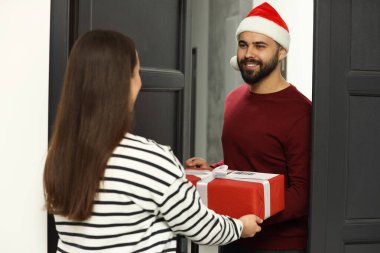 Noel Baba şapkalı bir kurye, genç bir bayana evde Noel hediyesi veriyor. E- posta ile hediye gönderiliyor