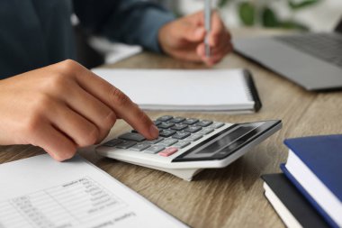 Ahşap masada not alırken hesap makinesi kullanan kadın, yakın plan