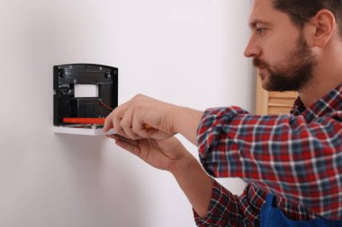 Teknisyen beyaz duvarlara ev güvenlik alarmı kuruyor.