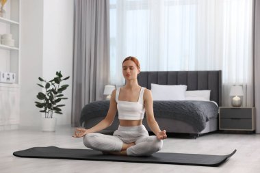 Evdeki yoga minderinde Padmasana egzersizi yapan güzel genç bir kadın. Lotus pozu