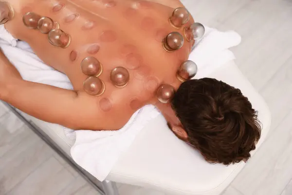 Cupping therapy. Man with glass cups on massage couch indoors, top view