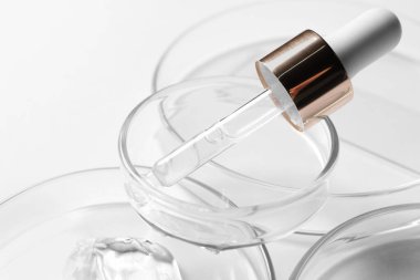 Beyaz arka planda kozmetik serumu ve pipeti olan petri kapları, yakın plan.