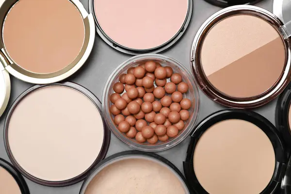 Different face powders on grey background, flat lay