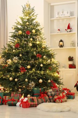 Noel ağacının altında bir sürü hediye kutusu süs süsleri ve oda ışıklarıyla süslenmiş.