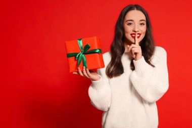 Kırmızı arka planda Noel hediyesi olan güzel genç bir kadın. Mesaj için yer var.