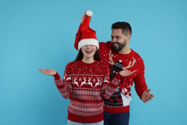 Açık mavi arka planda Noel süveteri giyen mutlu genç çift
