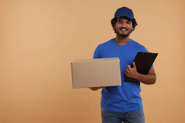 Happy courier with parcel and clipboard on light brown background, space for text