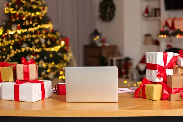 Modern laptop and Christmas gifts on table at home
