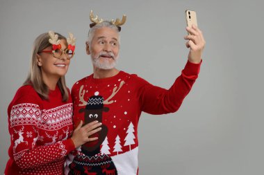 Yılbaşı süveteri, ren geyiği saç bandı ve gri arka planda selfie çeken son sınıf çifti. Metin için boşluk