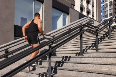 Güneşli bir günde merdivenlerden koşarak çıkan bir adam.