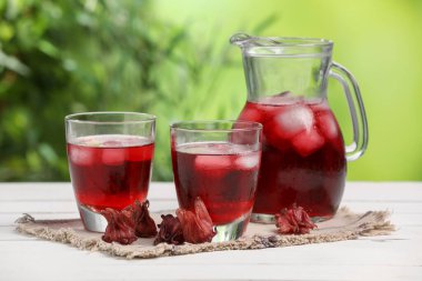 Beyaz ahşap masada, bulanık yeşil arka planda buz küpleri ve gül çiçekleri ile amber çayını tazeliyorum.