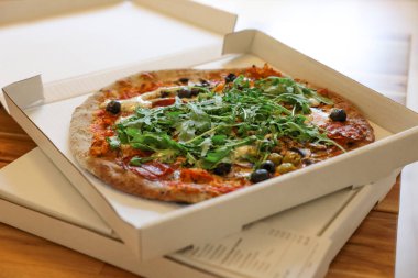 Arugula, mantar ve zeytinli nefis pizza, ahşap masada, yakın plan.