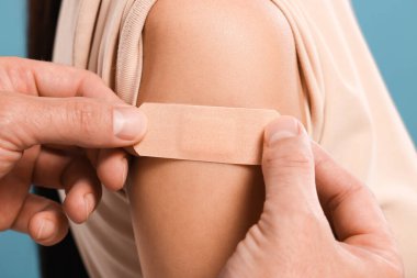 Doktor açık mavi arka plana karşı aşıdan sonra kadının koluna alçı yapıştırıyor.