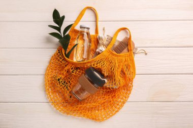 Beyaz ahşap masa üzerinde farklı eşyaların bulunduğu ağ torbası, üst manzara. Bilinçli tüketim