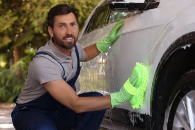 Worker washing auto with sponge at outdoor car wash