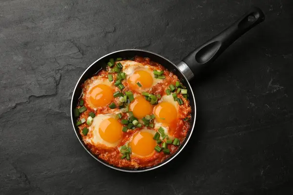 Delicious Shakshuka in frying pan on black textured table, top view
