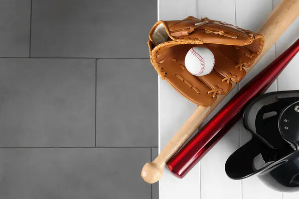 Baseball bats, batting helmet, leather glove and ball on white wooden bench indoors, top view. Space for text
