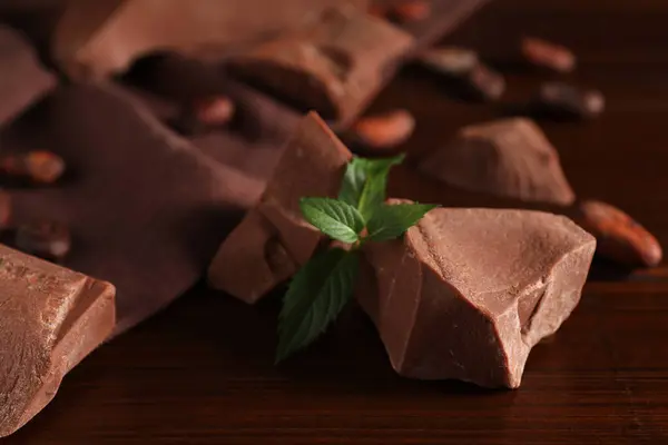 Pieces of tasty milk chocolate and mint on wooden table, closeup