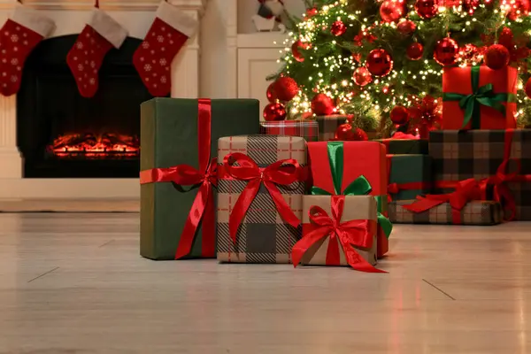 Many gift boxes near decorated Christmas tree and fireplace indoors