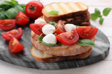 Beyaz ahşap masada mozarella, domates, fesleğen ve pesto soslu lezzetli Caprese sandviçi.