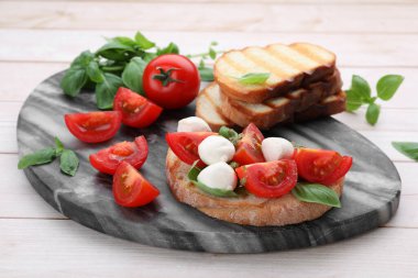 Beyaz ahşap masada mozarella, domates, fesleğen ve pesto soslu lezzetli Caprese sandviçi.