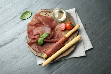 Lezzetli bresaola, domates, Grissini çubukları ve fesleğen yaprakları gri desenli masa, üst manzara