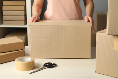 Paketleme malları. Kapalı alandaki beyaz masada karton kutuları olan bir kadın.