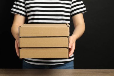 Siyah arka planda karton kutular tutan kadın, yakın plan. Paketleme malları