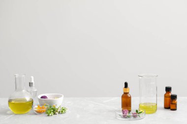 Kozmetik yağ, laboratuvar malzemesi ve çiçekler açık gri masada, metin için yer var.