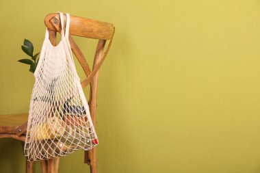 Bilinçli tüketim. Zeytin duvarının yanındaki sandalyede asılı ekolojik ürünlerin bulunduğu ağ torbası, mesaj için yer