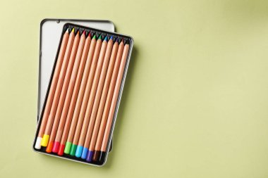 Açık zeytin arkaplan, üst görünüm ve metin için alan üzerine renkli pastel kalemler içeren bir kutu. Malzemeler çiziliyor