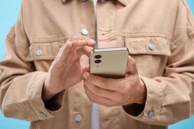 Genç adam açık mavi arka planda akıllı telefondan mesaj gönderiyor, yakın plan.