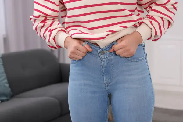 Woman trying to fit into her jeans at home, closeup