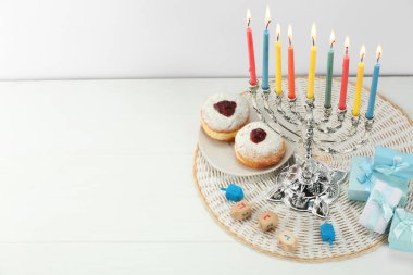 Hanuka kutlaması. Beyaz ahşap masada yanan mumlar, dreideller, çörekler ve hediye kutuları olan Menorah, metin için yer