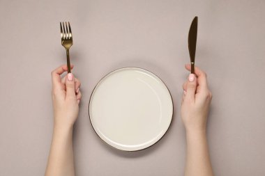 Bej masadaki boş tabağın yanında çatal ve bıçak tutan kadın.