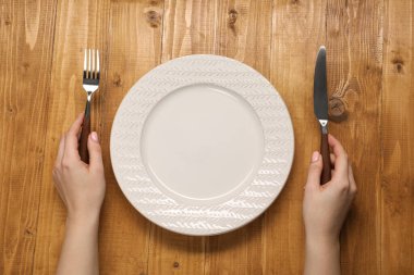 Ahşap masada çatal ve bıçak taşıyan bir kadın.