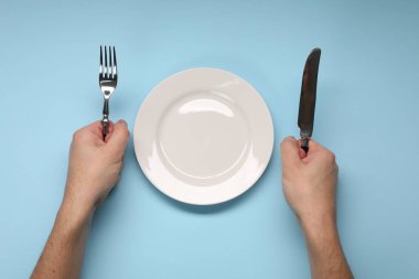 Çatal ve bıçak tutan adam boş tabağın yanında açık mavi masada, üst tarafta.