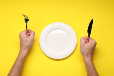 Sarı masadaki boş tabağın yanında çatal ve bıçak tutan adam.